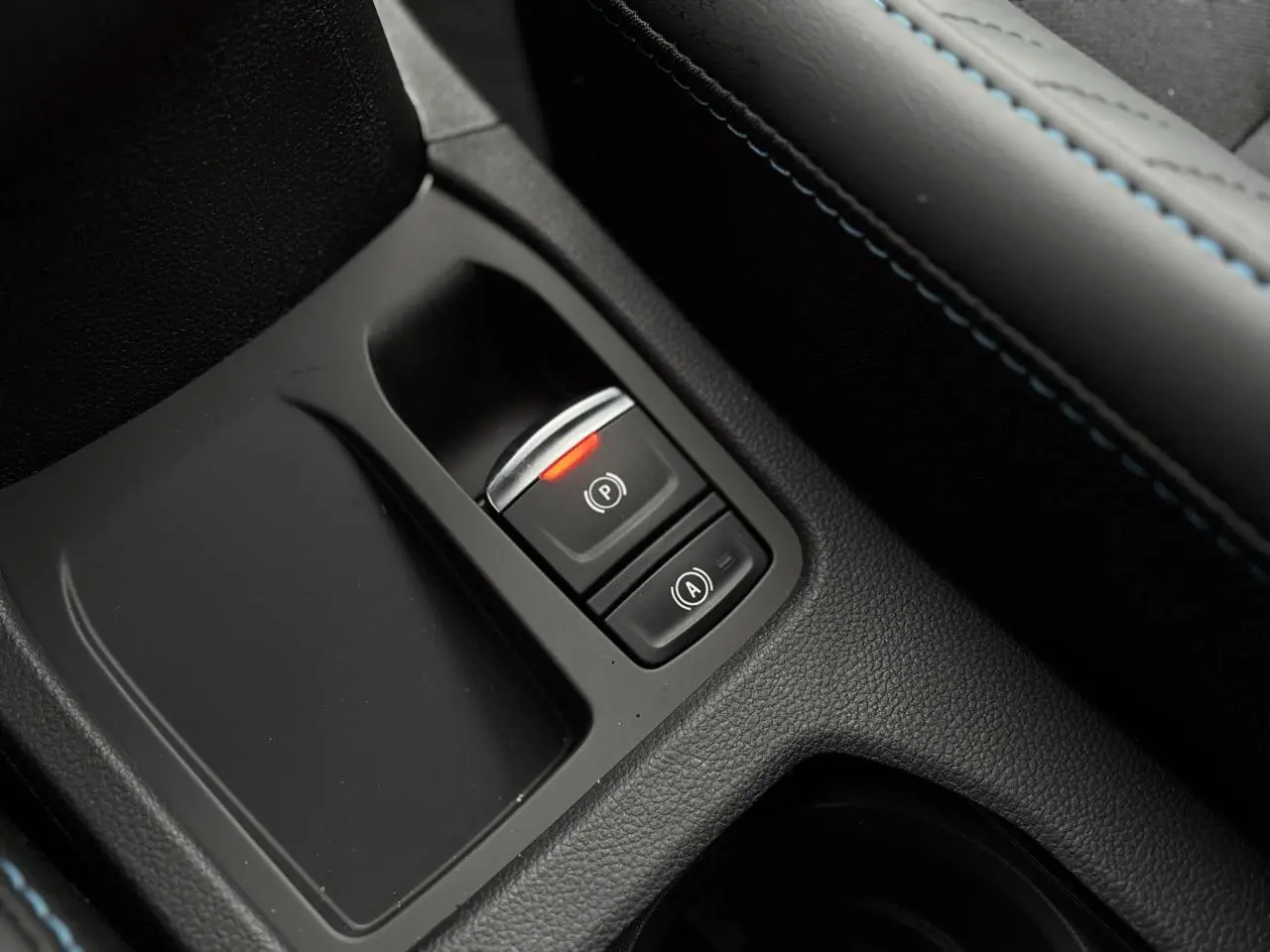 Gros plan sur la console centrale noire avec bouton frein à main électronique allumé et surpiqûres bleues Renault Clio 2025