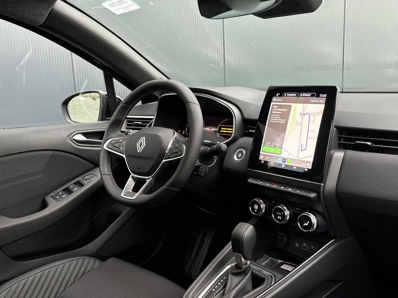 Intérieur avant Renault Clio 2025 noir, volant multifonction, écran tactile vertical et console centrale avec boîte auto.