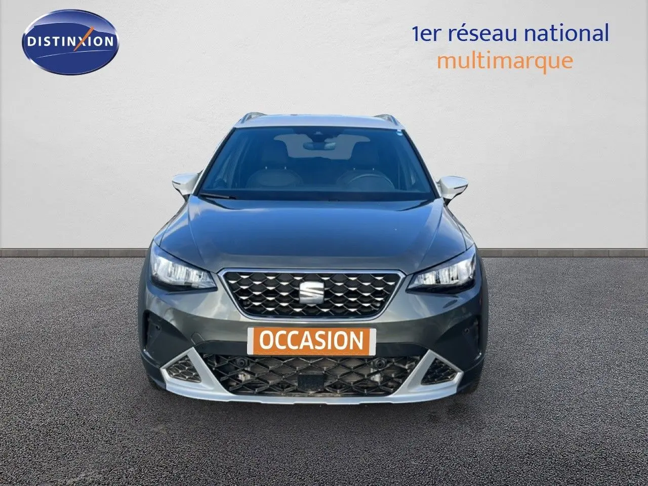 Vue frontale d'un SEAT Arona gris falaise métal avec toit blanc, calandre noire et plaque "OCCASION" orange.