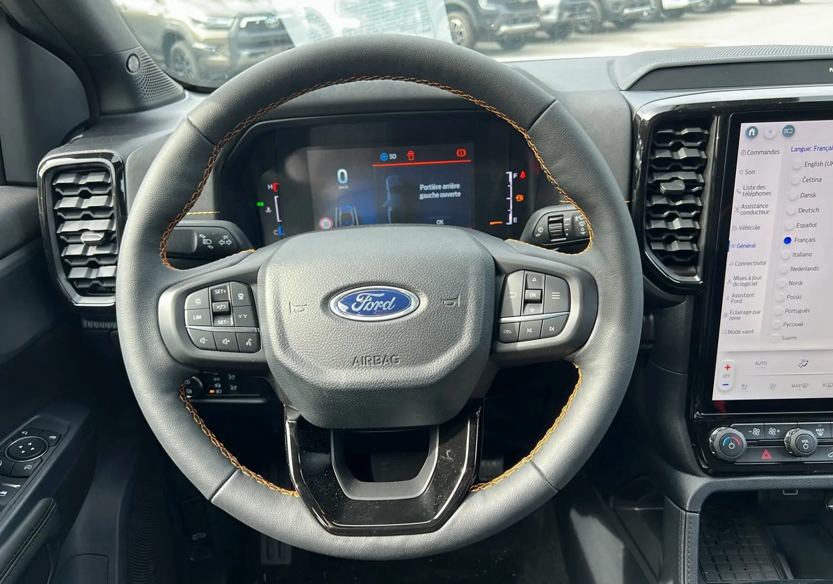 Vue frontale du volant cuir noir avec surpiqûres orange du Ford Ranger 2025, tableau de bord numérique et écran tactile central.