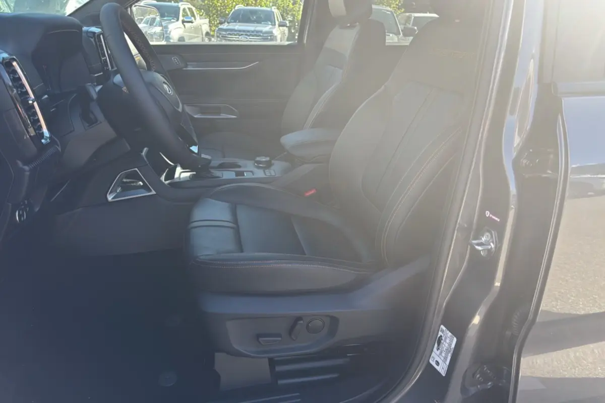 Vue intérieure côté conducteur du Ford Ranger Wildtrak 2026 gris carbone, sièges cuir noirs avec surpiqûres orange.