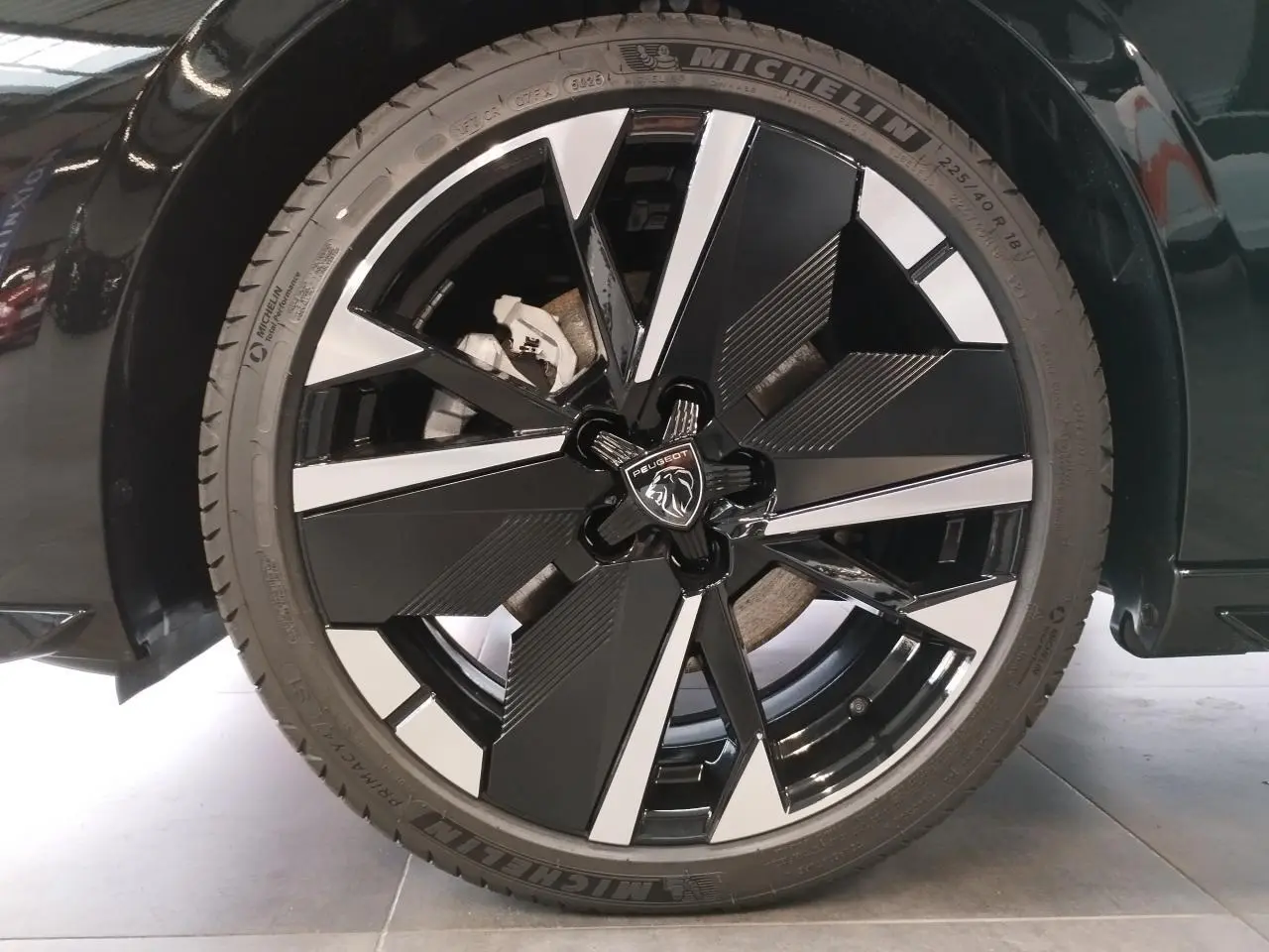 Gros plan sur la jante alliage 18 pouces bi-ton noir et argent de la Peugeot 308 noire métallisée, avec logo lion central.