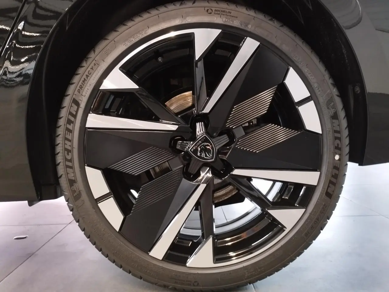 Gros plan sur la jante alliage bi-ton noir et argent avec logo Peugeot, montée sur une Peugeot 308 noire métallisée.