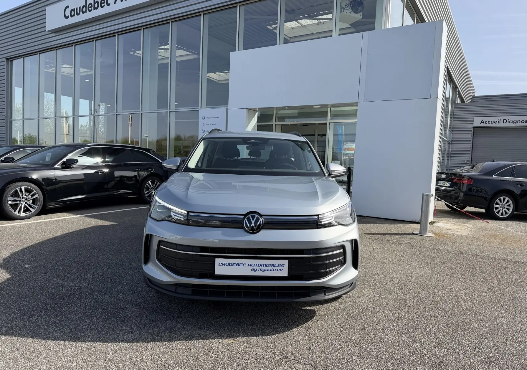 Volkswagen Tiguan gris vue de face, avec calandre noire et phares LED allumés devant un showroom.