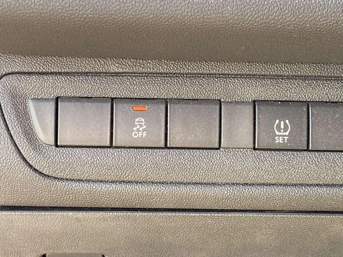 Gros plan sur les boutons de contrôle du système de stabilité et du réglage de pression des pneus dans une Peugeot 208 noire de 2015.