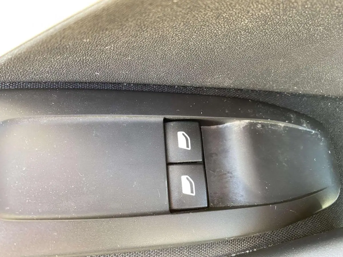 Gros plan sur les boutons de lève-vitres avant électriques noirs dans une Peugeot 208 noire de 2015.