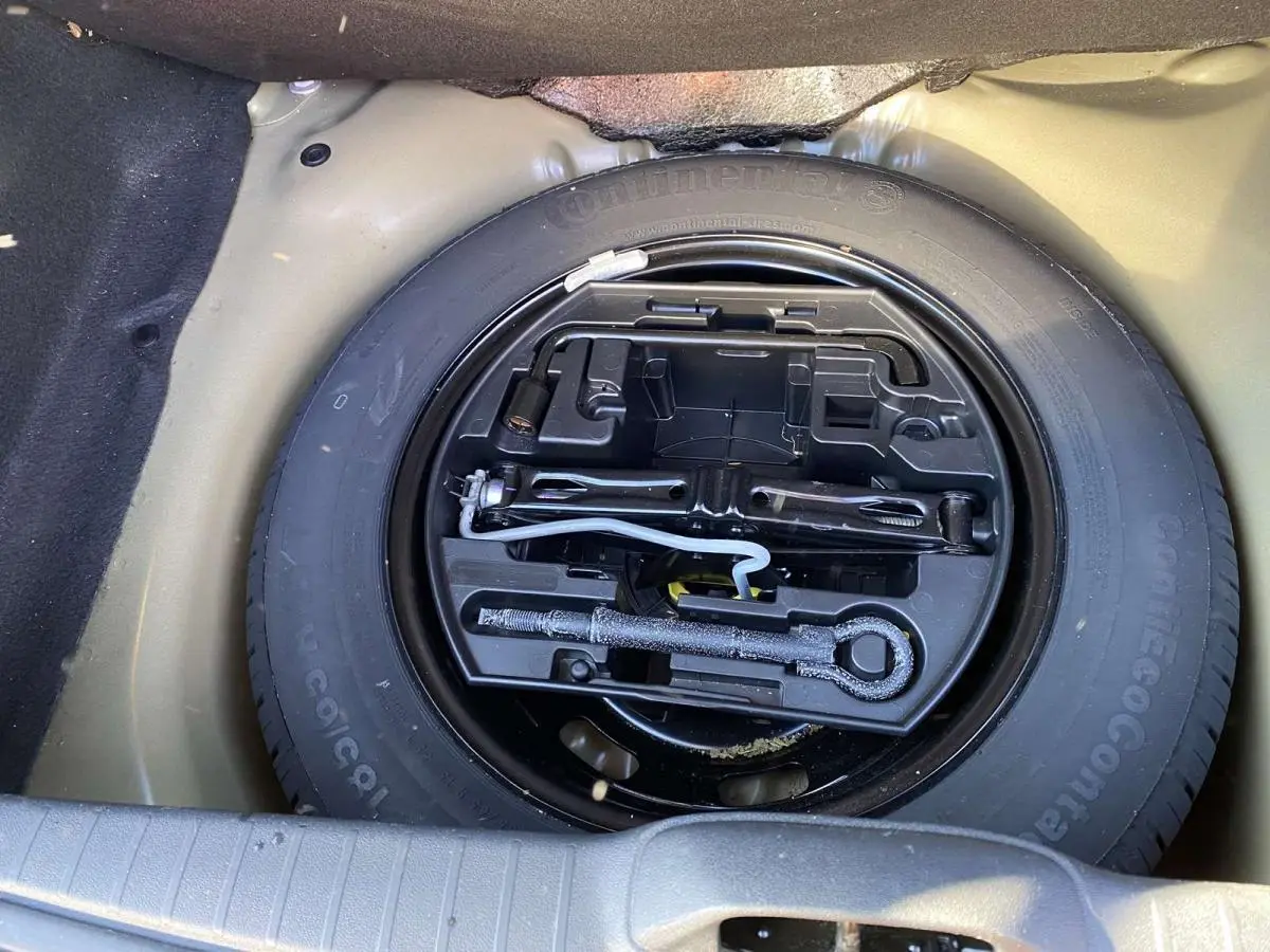 Roue de secours acier 15 pouces avec outils de bord dans le coffre d'une Peugeot 208 noire de 2015.