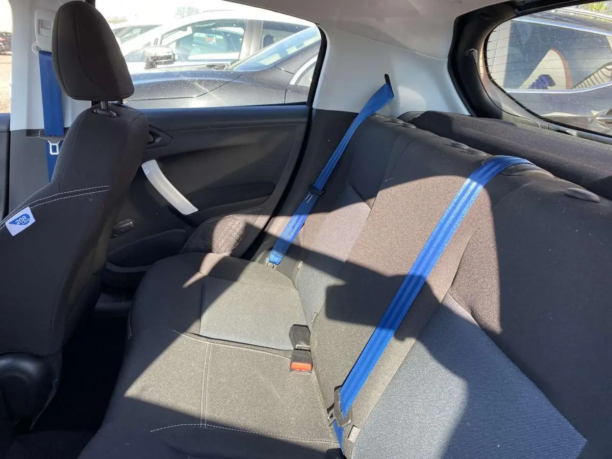 Vue intérieure arrière droite du Peugeot 208 noir de 2015, avec ceintures de sécurité bleues et sièges tissu noir.