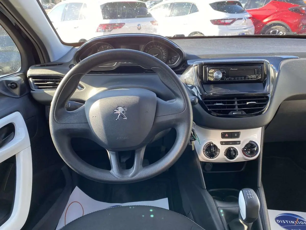 Vue intérieure du poste de conduite d'une Peugeot 208 noire de 2015, avec volant, tableau de bord et autoradio Pioneer visible.