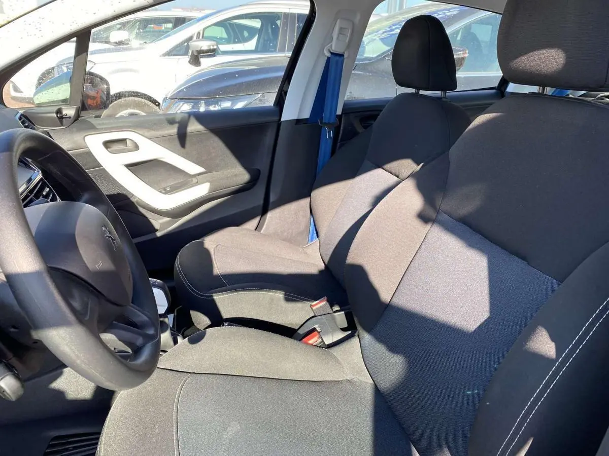 Intérieur avant droit de la Peugeot 208 noire 2015, sièges tissu gris et volant visible côté conducteur.