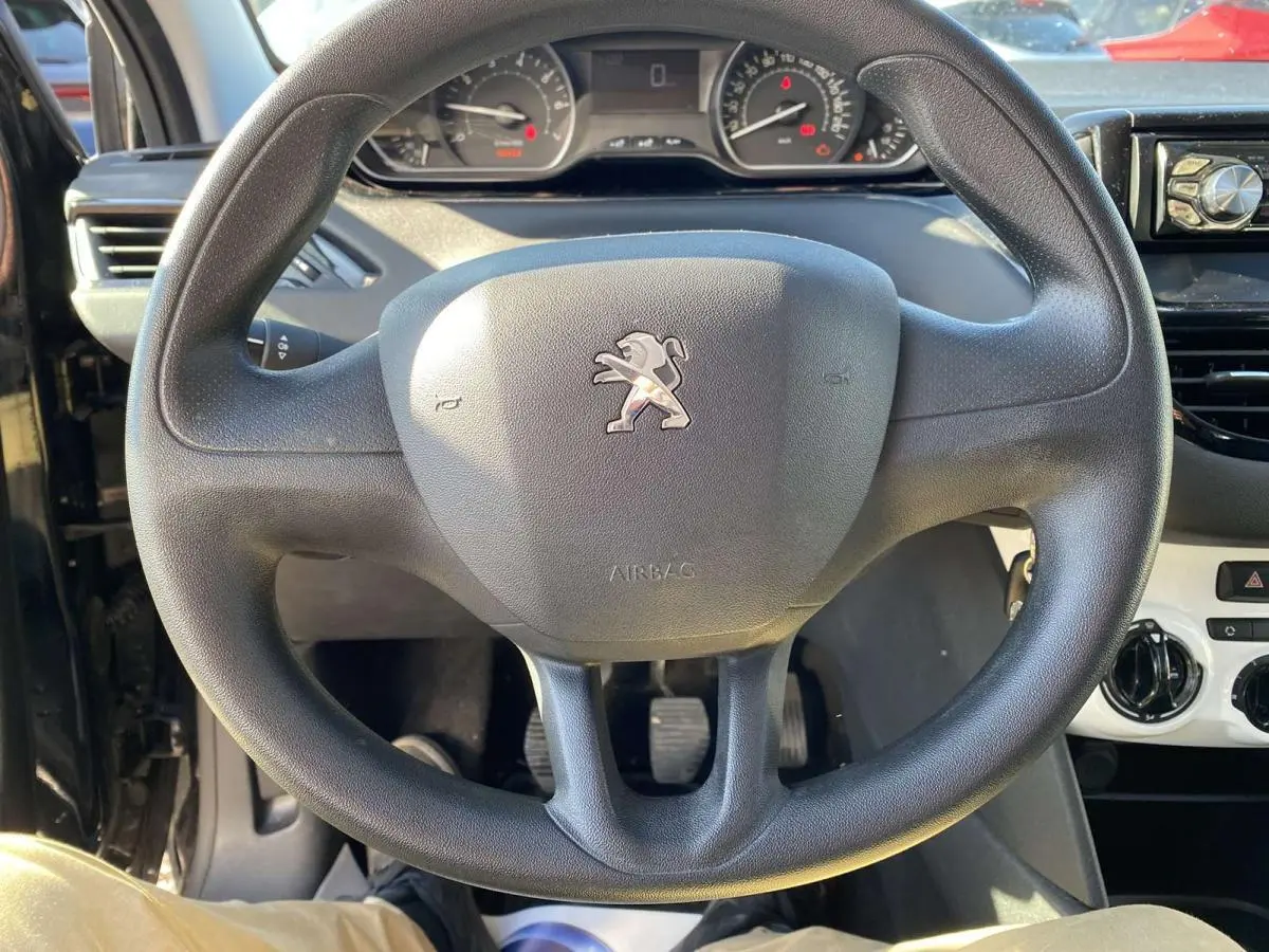 Volant noir de Peugeot 208 2015 essence, vue de face centrée sur le logo lion et le tableau de bord.