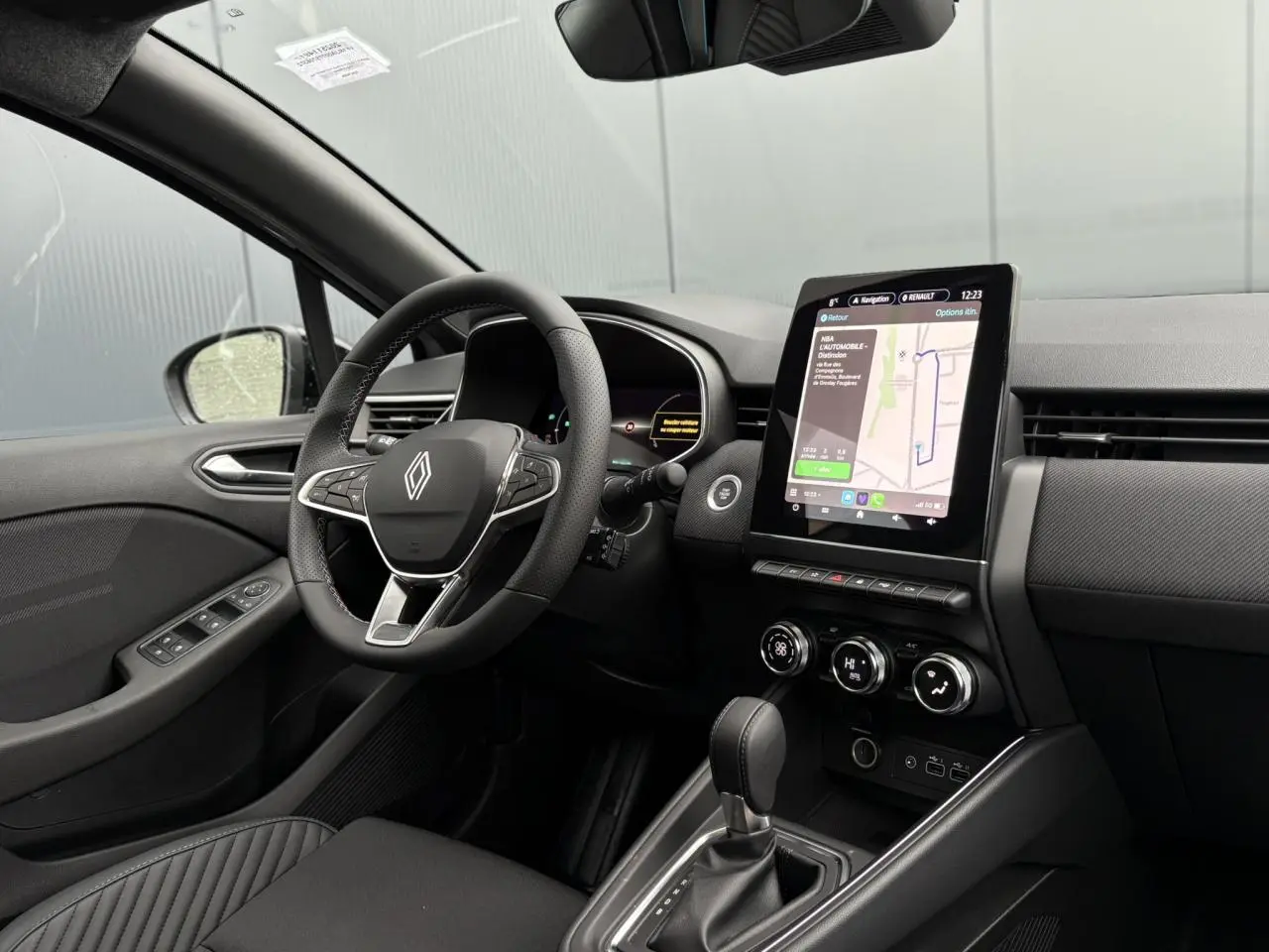 Vue intérieure côté conducteur de la Renault Clio 2025 avec tableau de bord noir et écran tactile central vertical.