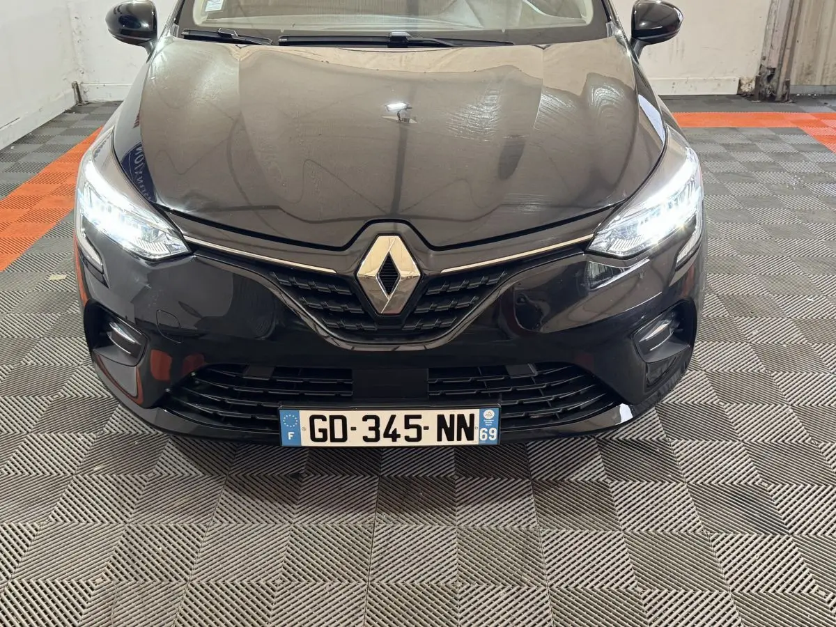 Vue avant rapprochée d’une Renault Clio Business E-Tech hybride noire avec phares LED allumés dans un garage.