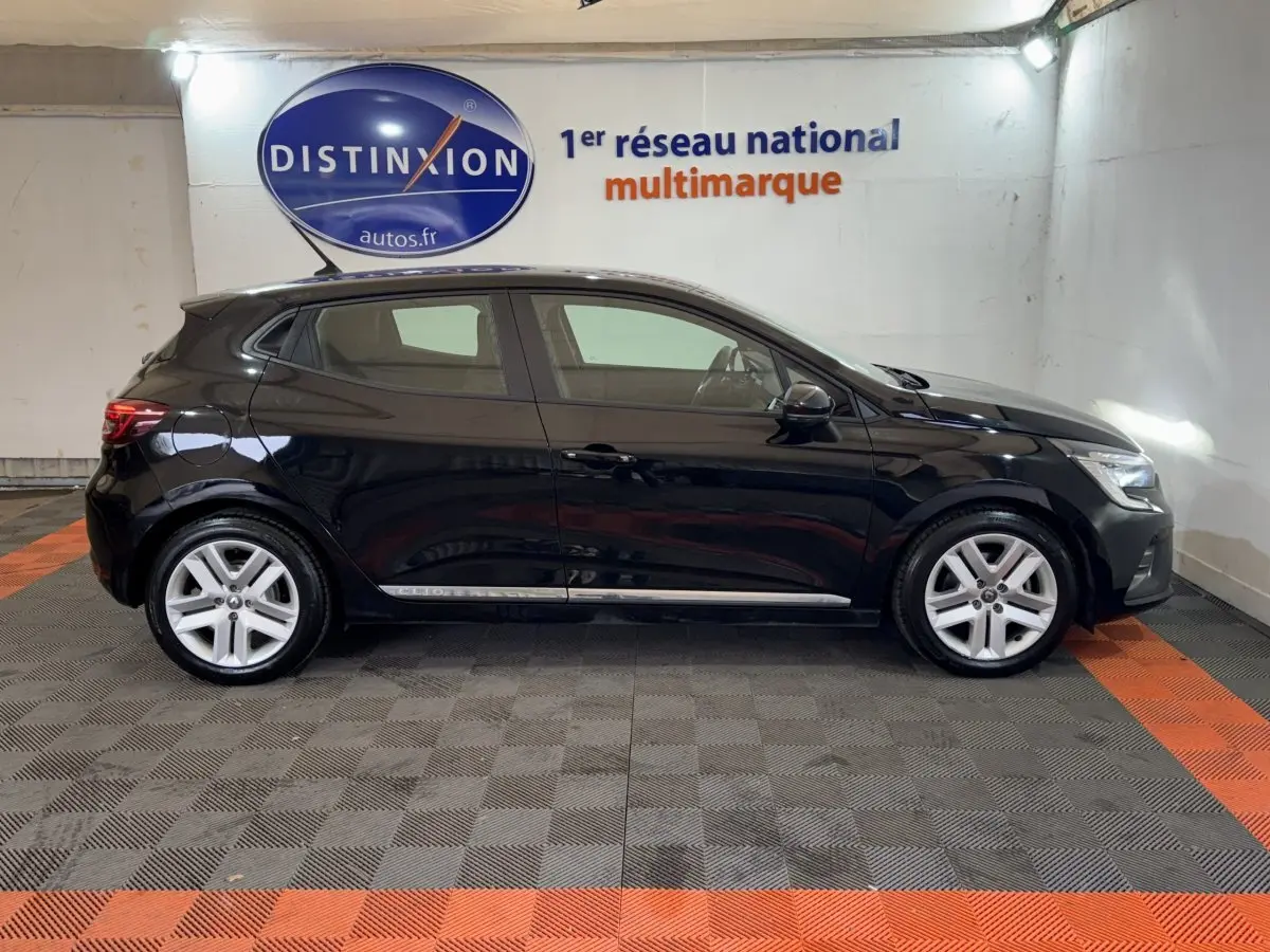 Profil côté gauche d'une Renault Clio Business E-Tech hybride noire 2021, stationnée en intérieur sur sol gris et orange.