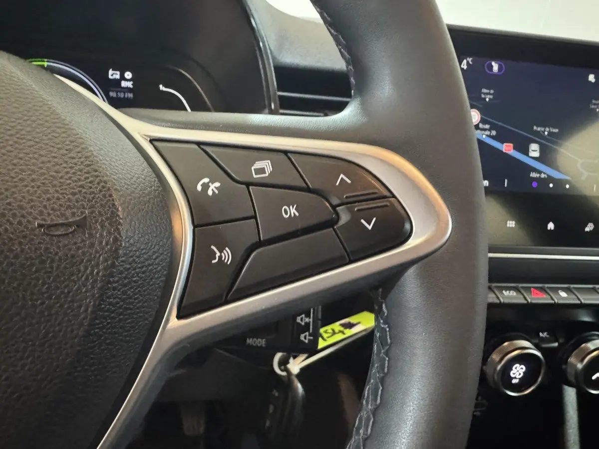 Gros plan sur le volant cuir synthétique noir de la Renault Clio Business E-Tech avec commandes multifonctions et écran tactile en arrière-plan.