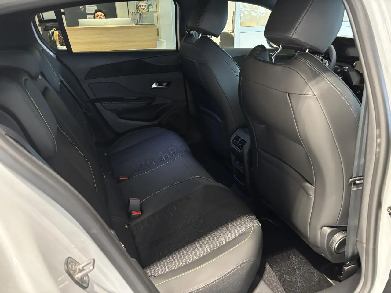 Vue intérieure arrière côté gauche de la Peugeot 308 blanche 1.2i Hybrid avec sellerie noire et surpiqûres vert Adamite.