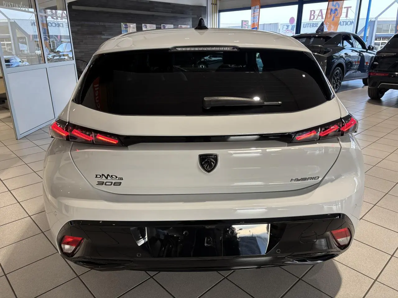 Vue arrière d'une Peugeot 308 hybride blanche avec feux arrière LED en forme de griffes et bandeau noir brillant.
