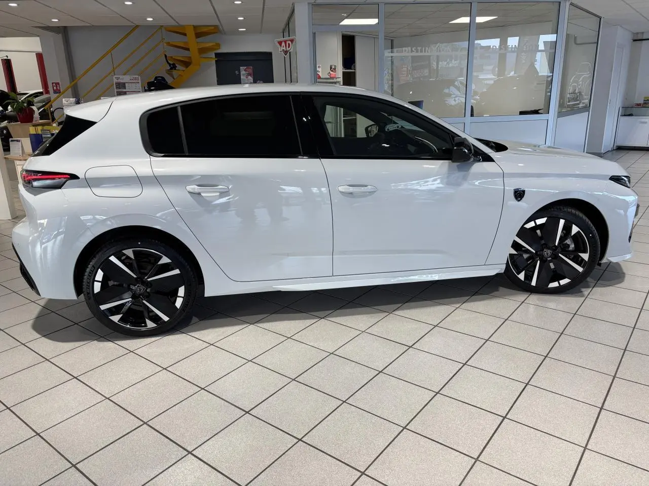 Vue de profil côté gauche d'une Peugeot 308 blanche hybride avec jantes alliage bi-ton et vitres surteintées en showroom.
