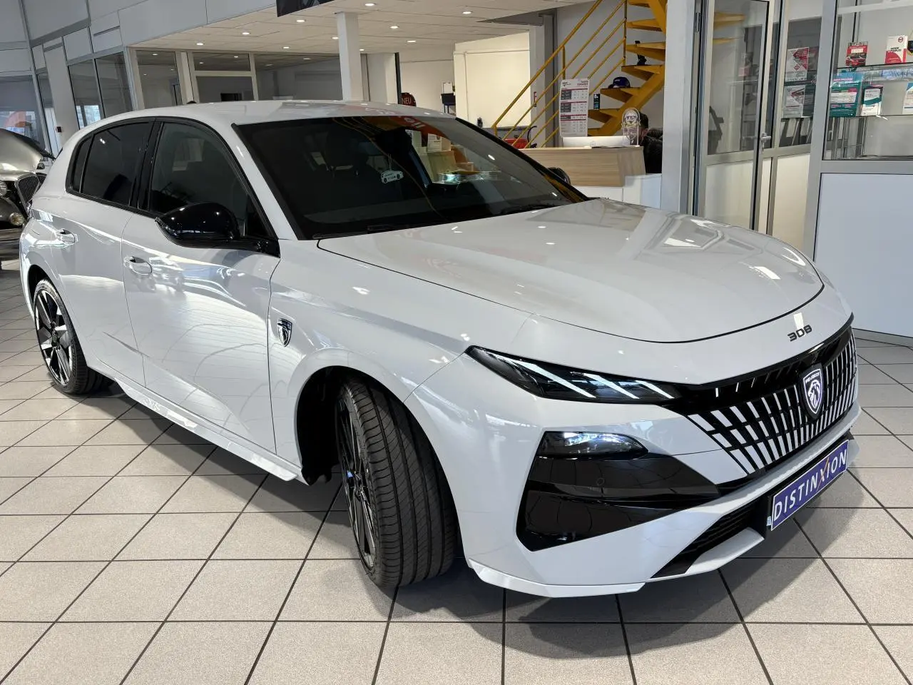 PEUGEOT 308 hybride blanche vue 3/4 avant droit en showroom avec calandre noire distinctive et jantes bi-ton.