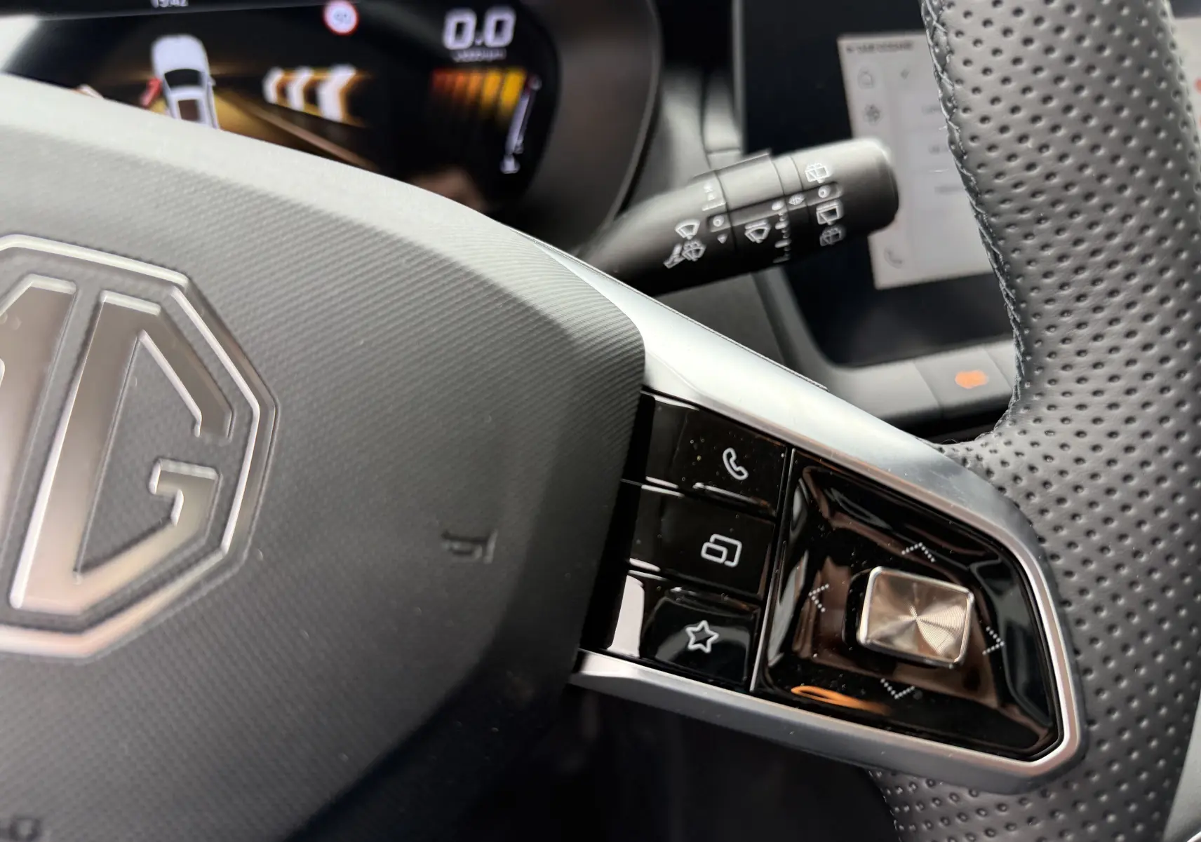 Gros plan sur le volant noir perforé du MG ZS 2026, avec commandes multifonctions et logo MG au centre.