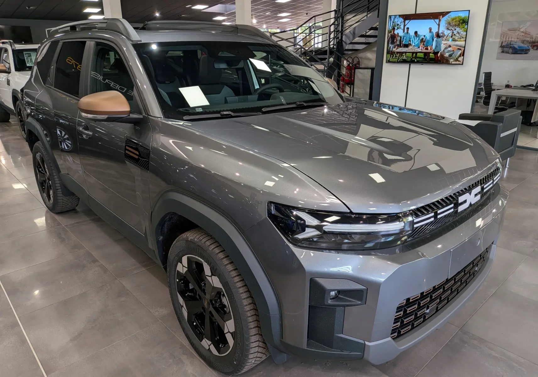 SUV Dacia Bigster Hybrid-G 150 4x4 gris schiste vu en 3/4 avant droit avec rétroviseurs bronze et jantes noires.