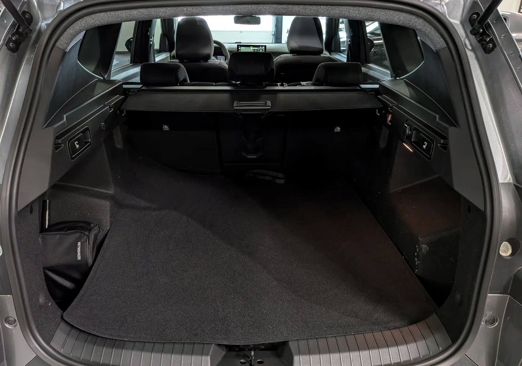 Coffre ouvert d’un Dacia Bigster Hybrid-G 150 4x4 gris schiste, vue intérieure arrière montrant l’espace de chargement et la plage arrière.