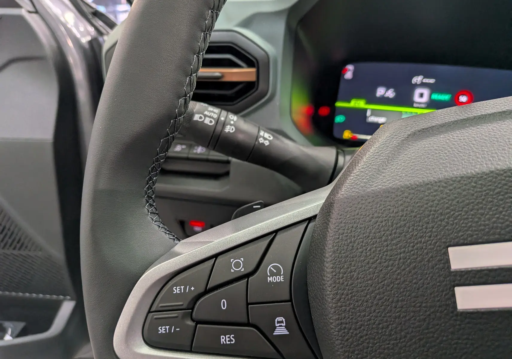 Gros plan sur le volant noir et les commandes multifonctions du DACIA BIGSTER Hybrid-G 150 4x4, tableau de bord numérique en arrière-plan.
