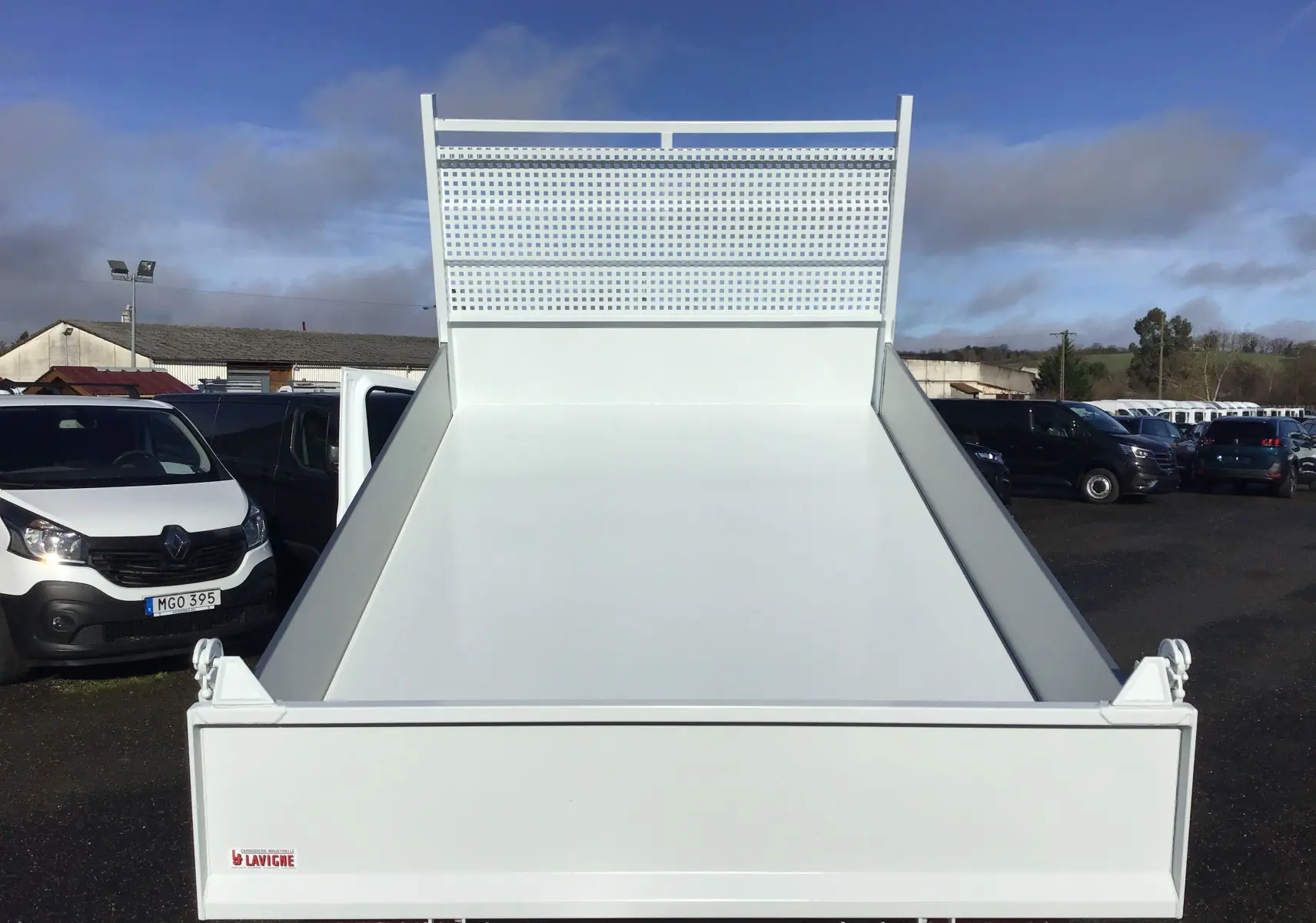 Vue arrière frontale d'une benne blanche Ford Transit Châssis Cabine 2024, avec ridelle relevée et grille de protection.