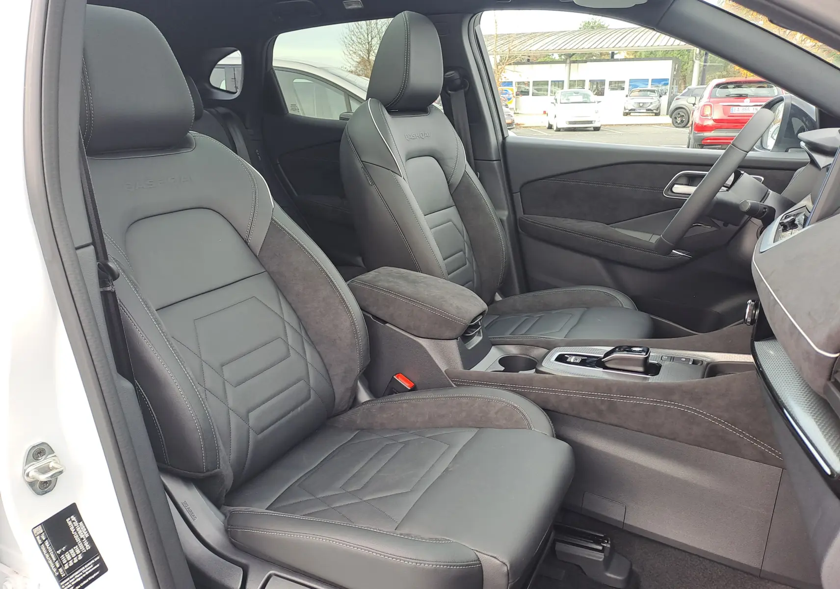 Vue intérieure côté gauche du Nissan Qashqai 2025, sièges cuir noir avec surpiqûres blanches et console centrale en alcantara.