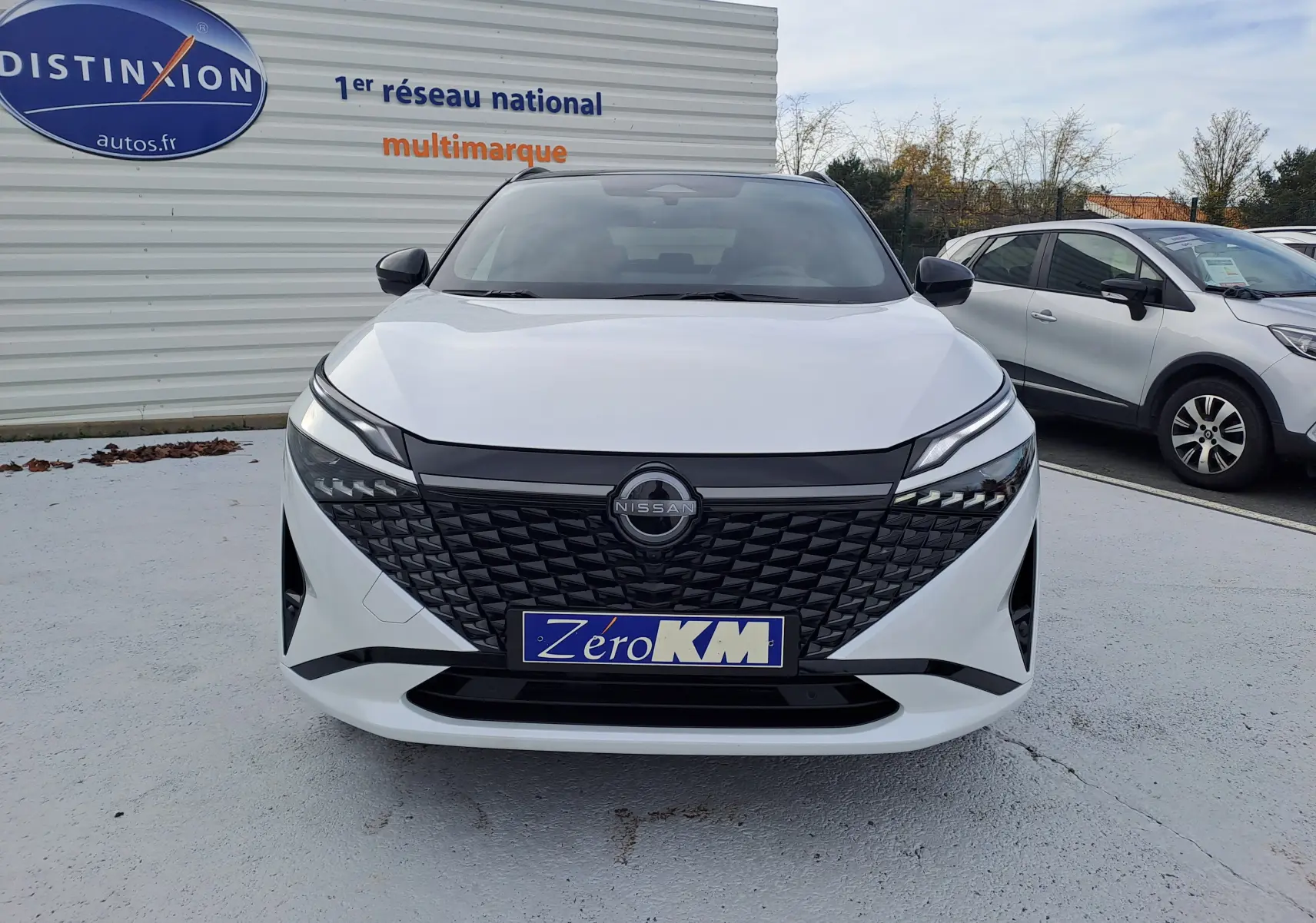 Vue frontale d'un Nissan Qashqai blanc nacré avec toit noir, calandre noire texturée et phares LED distinctifs.