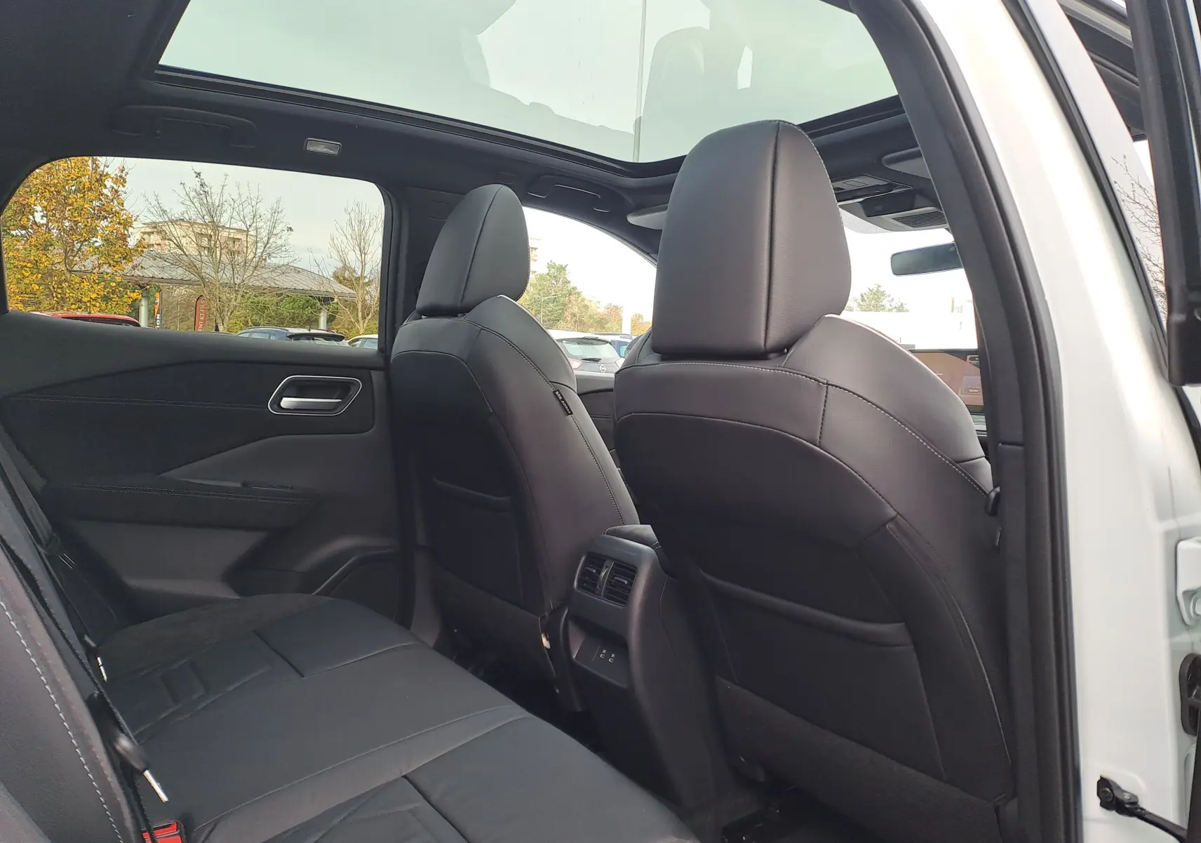 Vue intérieure arrière du Nissan Qashqai 2025 blanc nacré avec sièges noirs et toit panoramique en verre.