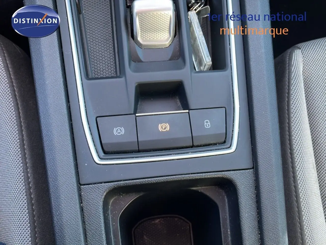 Gros plan sur la console centrale de la SEAT LEON 2025, avec boutons de frein à main électronique et rangement, intérieur gris.