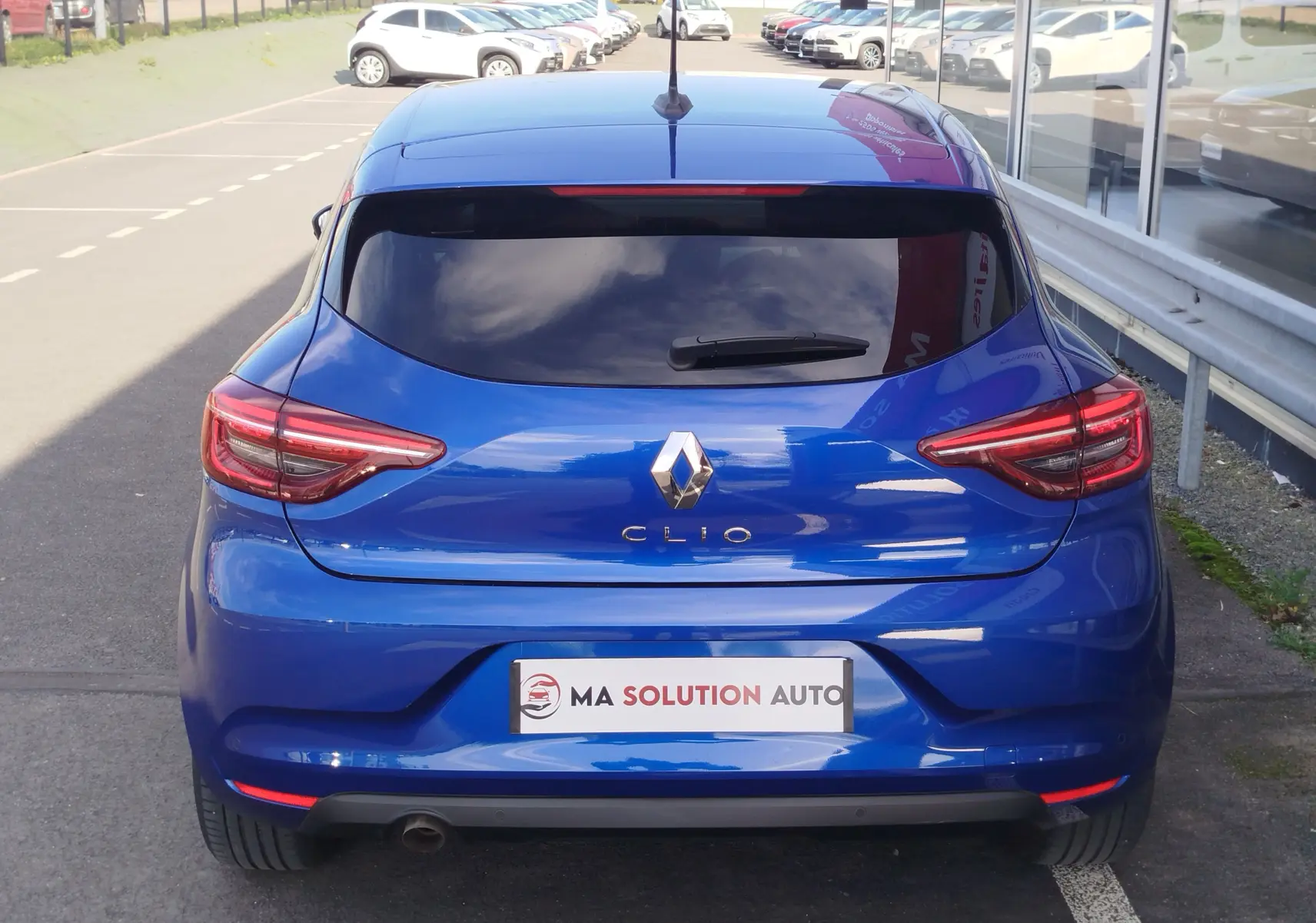 Vue arrière d'une Renault Clio 2022 Bleu Iron avec feux LED et lunette arrière teintée, stationnée près d'une vitrine.