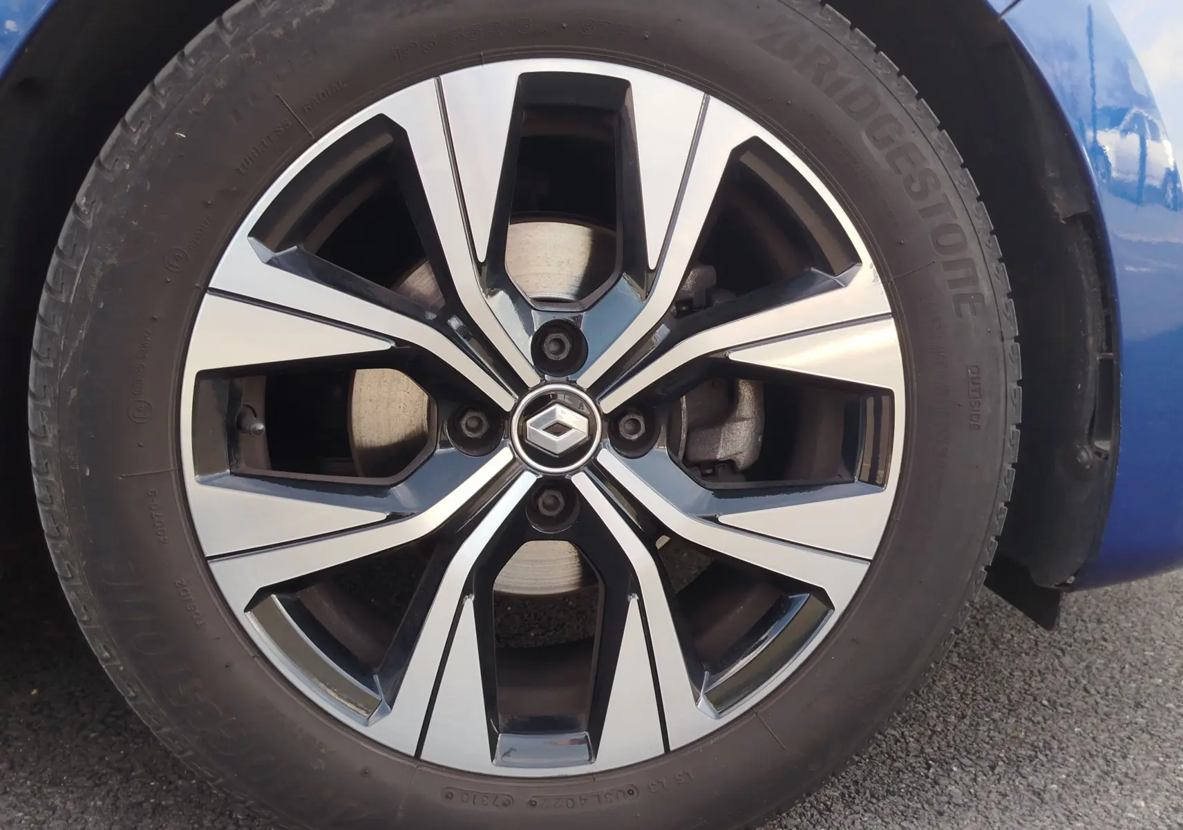 Gros plan sur la jante alliage bicolore noire et argentée d’une Renault Clio Bleu Iron, avec logo Renault au centre.