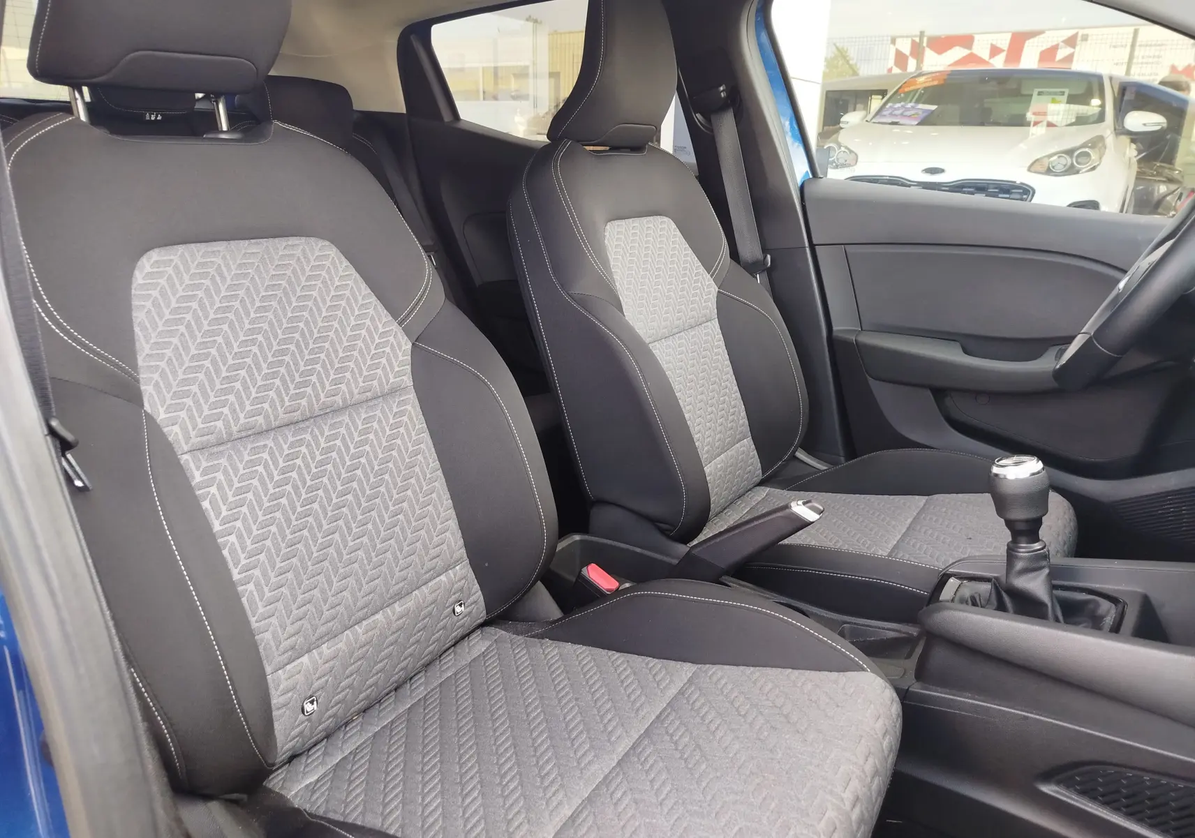 Vue intérieure côté gauche de la Renault Clio 2022 Bleu Iron, montrant les sièges avant en tissu gris à motifs géométriques.