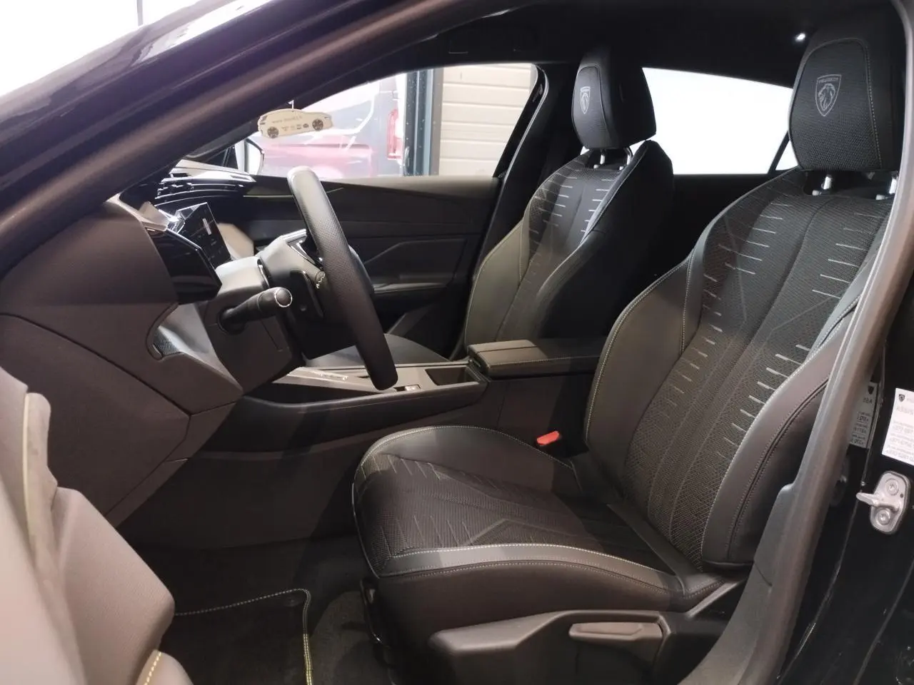 Vue intérieure côté conducteur de la Peugeot 308 noir métal, sièges tissu noir avec logo Peugeot brodé sur appuie-tête.