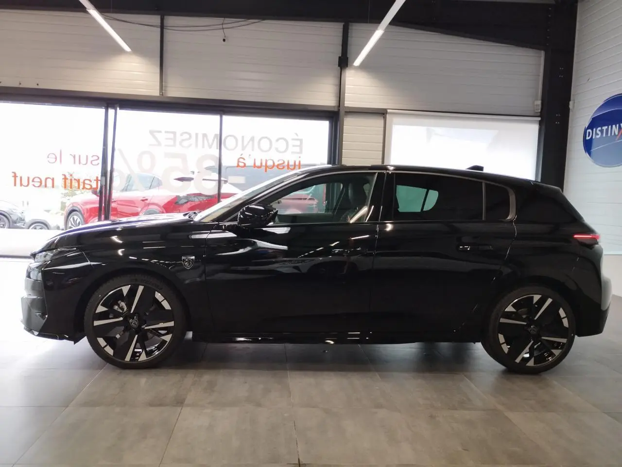 Profil côté gauche d'une Peugeot 308 noire métallisée avec jantes alliage bi-tons et blason distinctif sur l'aile avant.