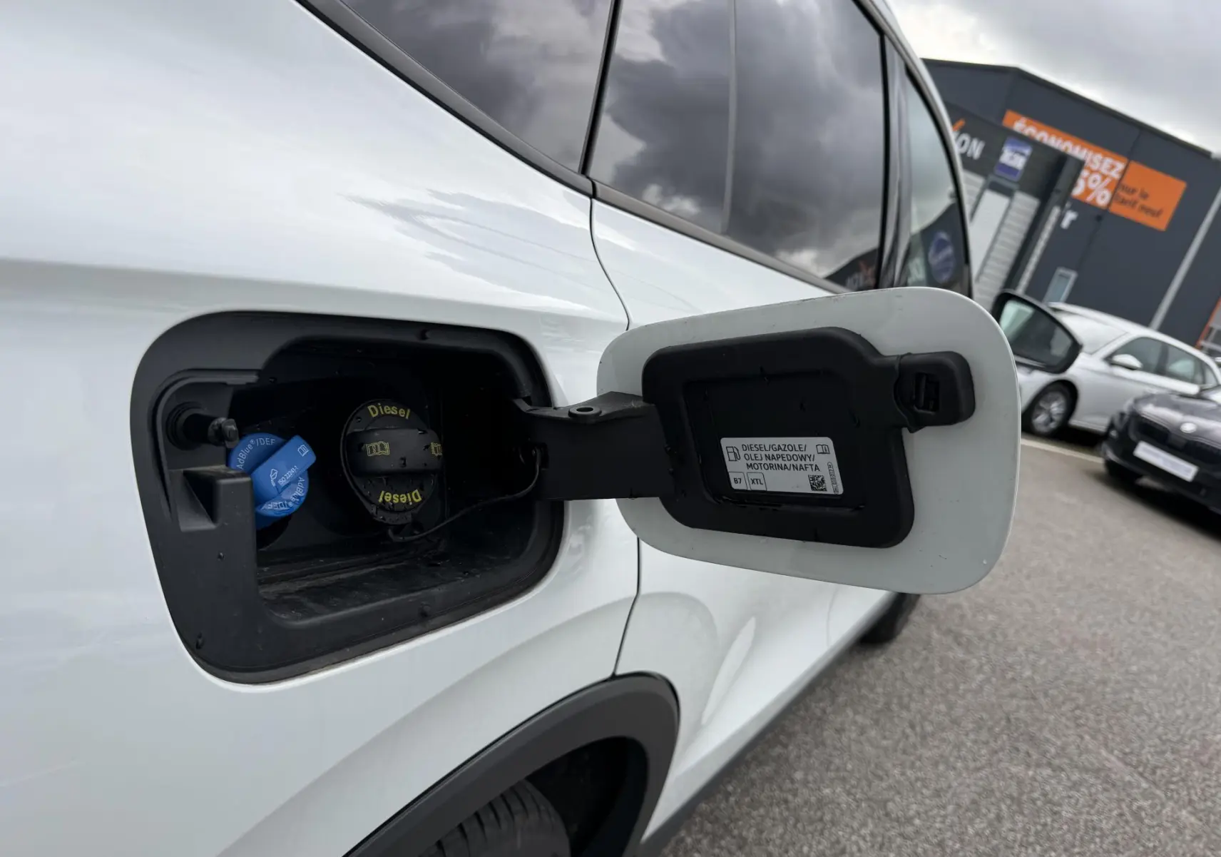 Vue rapprochée de la trappe à carburant ouverte côté gauche d’un Volkswagen Tiguan blanc avec bouchon diesel visible.