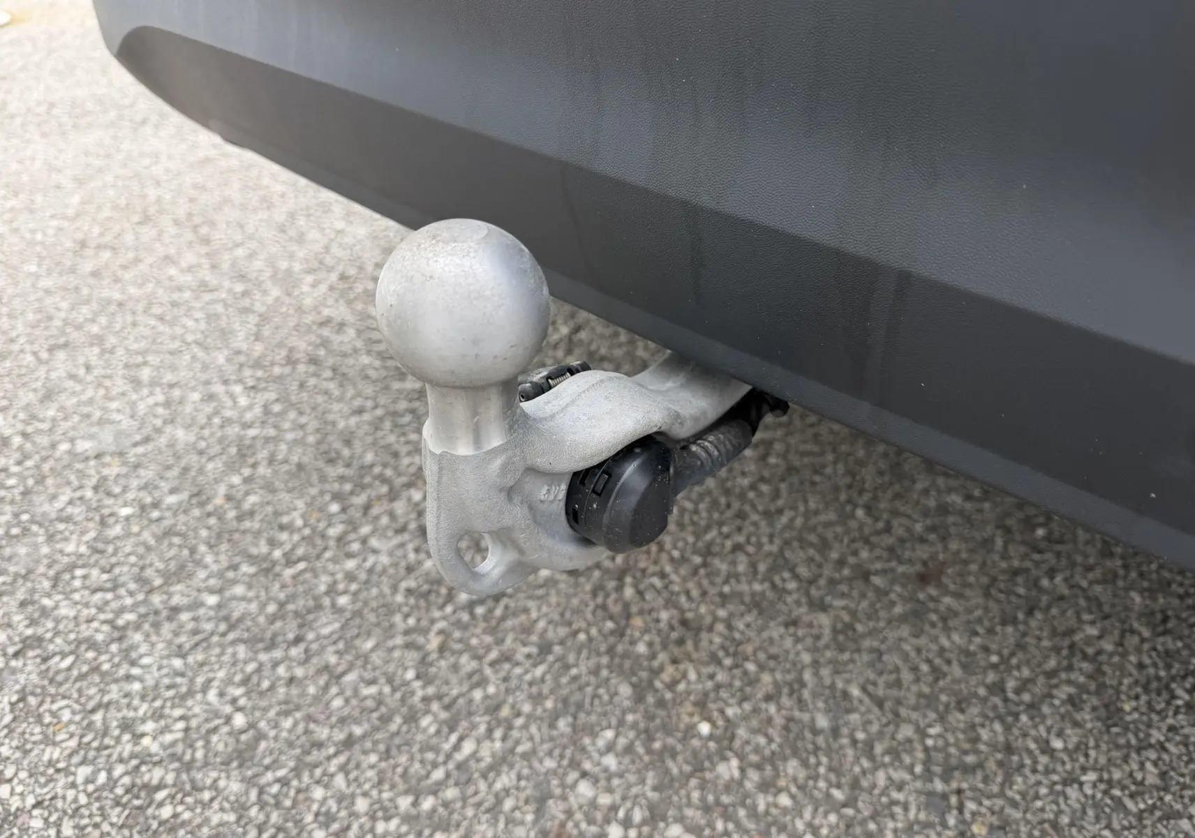 Gros plan sur l'attelage rabattable en métal gris sous le pare-chocs arrière noir d'un Volkswagen Tiguan blanc.