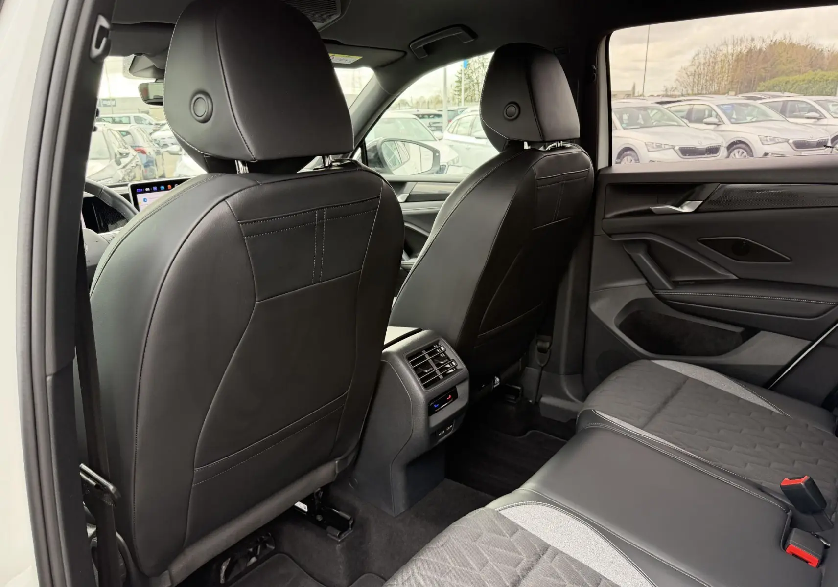 Vue arrière de l'intérieur du Volkswagen Tiguan 2025 blanc, sièges en cuir noir et tissu gris, avec console centrale et aérateurs.