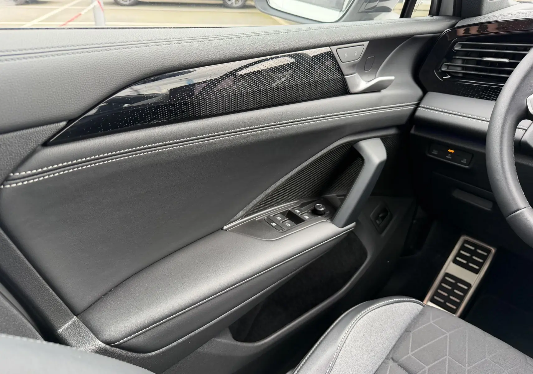 Vue intérieure côté conducteur du Volkswagen Tiguan 2025, avec garniture noire, surpiqûres blanches et commandes électriques.