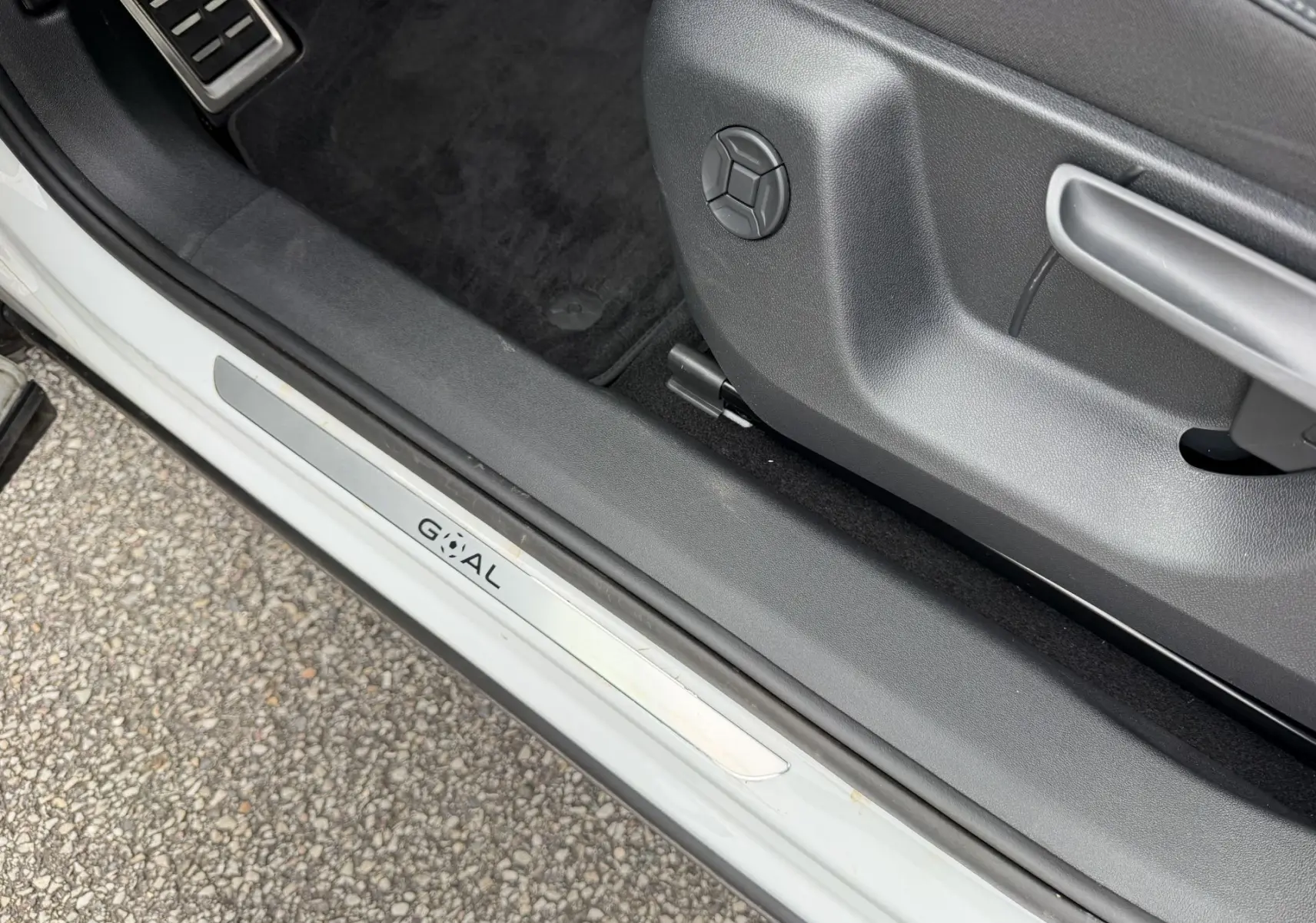 Gros plan sur la porte côté conducteur d’un Volkswagen Tiguan blanc, montrant la molette de réglage du siège et le seuil de porte.