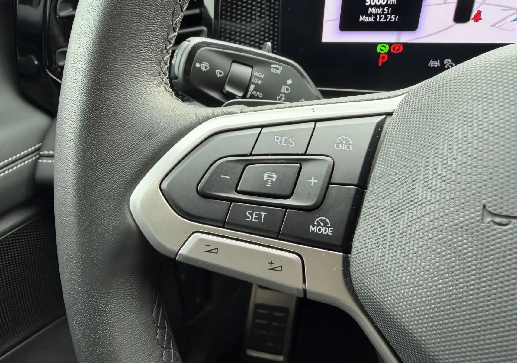 Gros plan sur les commandes multifonctions à gauche du volant cuir du Volkswagen Tiguan 2025 avec affichage digital en arrière-plan.