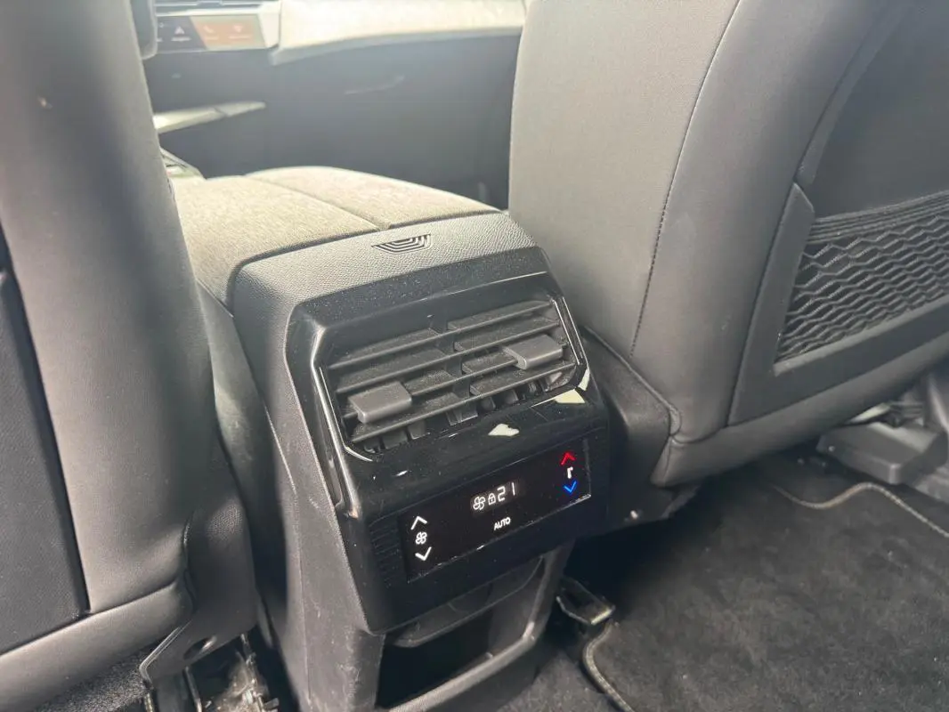 Vue rapprochée de la console arrière noire du Peugeot 5008 Hybrid 2025 avec commandes climatisation et sièges tissu.