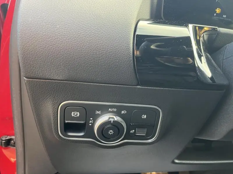Gros plan sur la commande des phares et frein de stationnement dans l'habitacle côté gauche d'une Mercedes GLA rouge Patagonie métallisé.