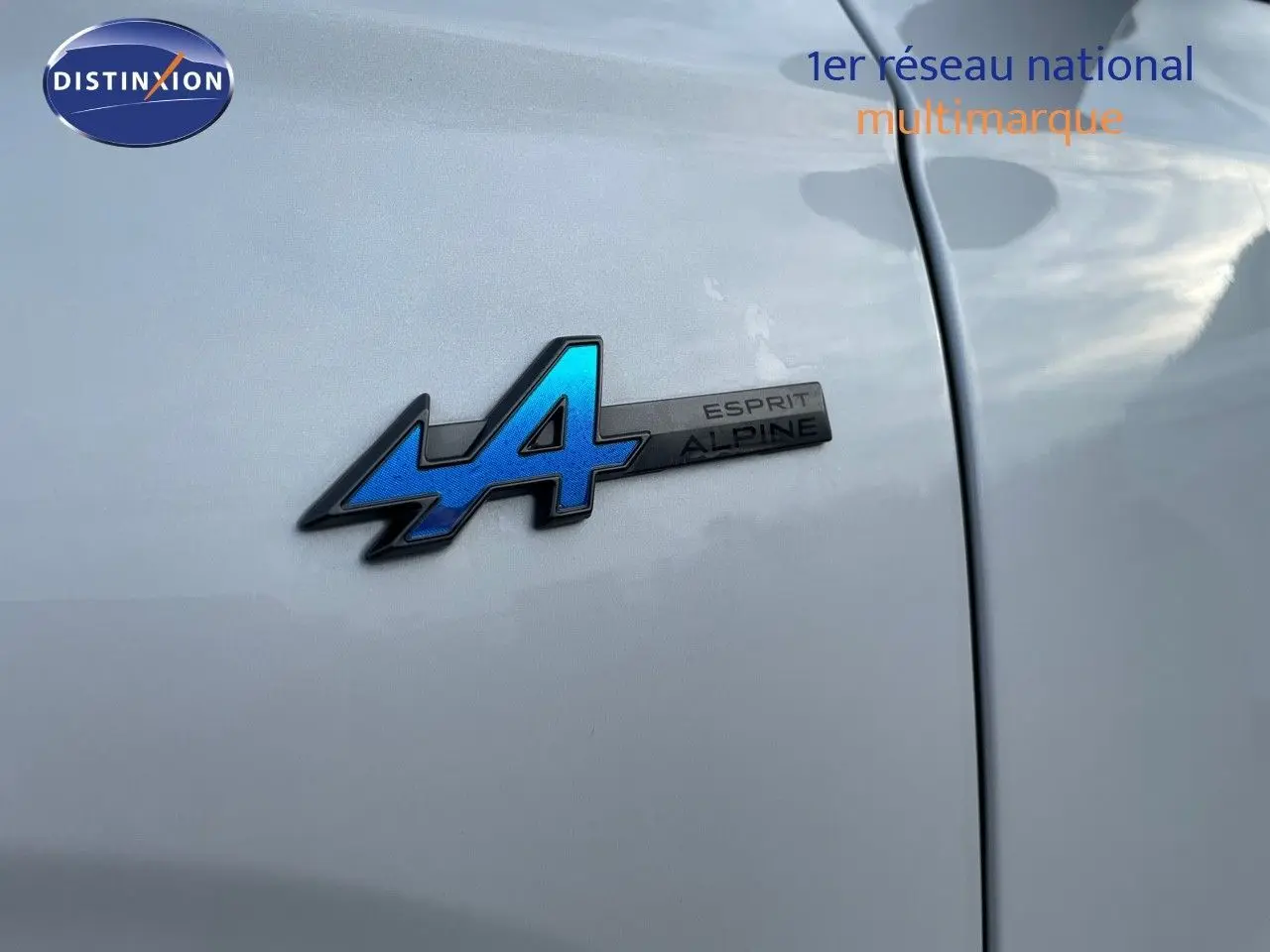 Gros plan sur l'écusson bleu Esprit Alpine sur la portière blanche nacrée d'un Renault Austral 2025 hybride.