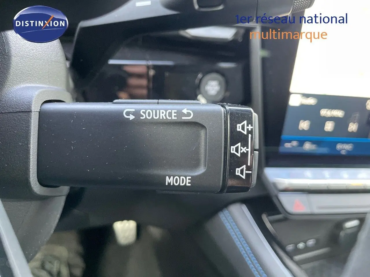 Gros plan sur la commande audio au volant du Renault Austral blanc nacré, avec tableau de bord et écran tactile en arrière-plan.