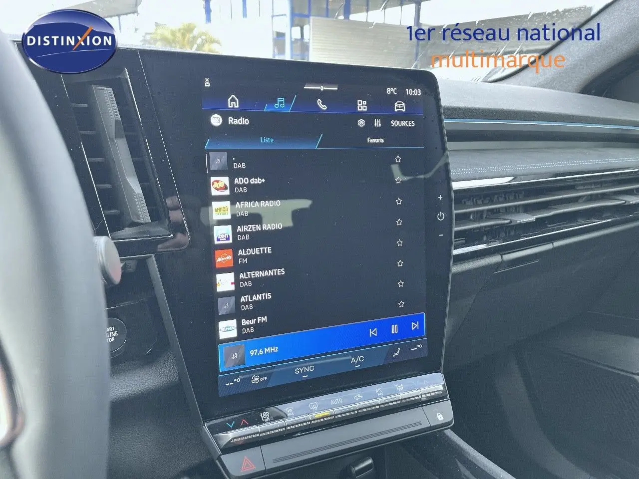 Vue intérieure centrée sur l'écran tactile du tableau de bord du Renault Austral blanc nacré 2025, affichant les stations radio.