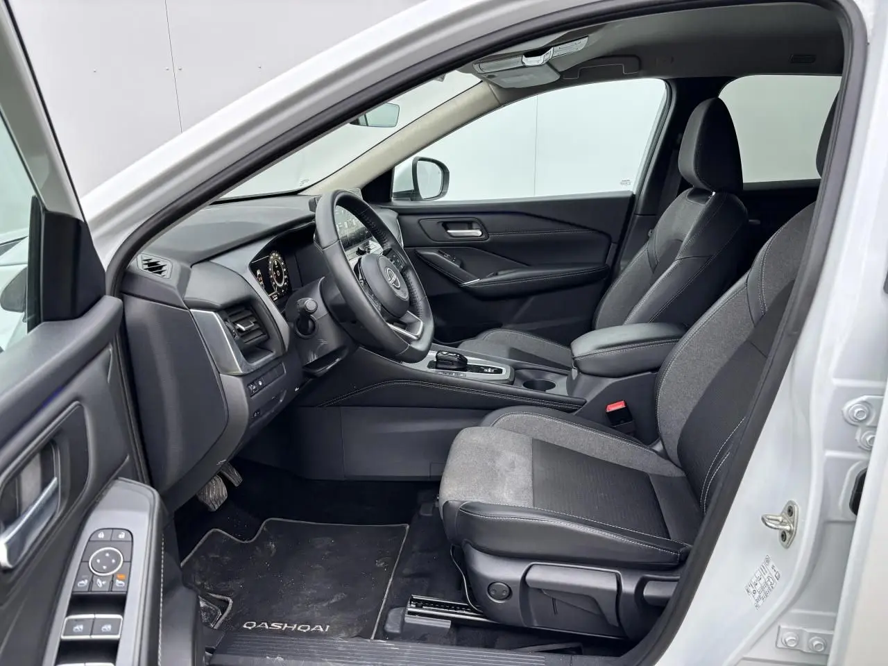 Vue intérieure côté conducteur du Nissan Qashqai blanc nacré 2025, avec sellerie mixte noire et tableau de bord moderne.
