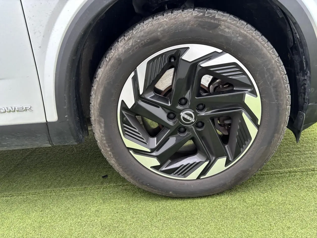 Gros plan sur la roue avant droite du Nissan Qashqai blanc nacré avec jante alliage noire et argentée.